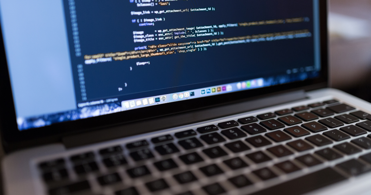 A imagem mostra um laptop aberto com a tela exibindo um editor de código em uma linguagem de programação, possivelmente PHP ou JavaScript, devido à sintaxe e às funções visíveis. O teclado do laptop é visível na parte inferior da imagem. A tela do laptop tem uma barra de tarefas na parte inferior com vários ícones de aplicativos. A imagem está focada na tela e no teclado, sugerindo um ambiente de trabalho de programação ou desenvolvimento de software.